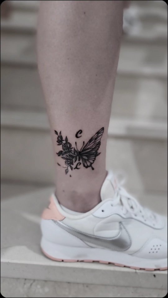Tatuaje de mariposa y flores en negro sobre el tobillo
